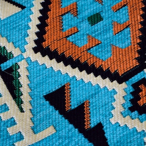 May include: Close-up of a blue, white, orange, green, and black woven fabric with a geometric pattern.
