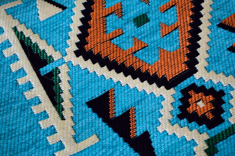 May include: Close-up of a blue, white, orange, green, and black woven fabric with a geometric pattern.
