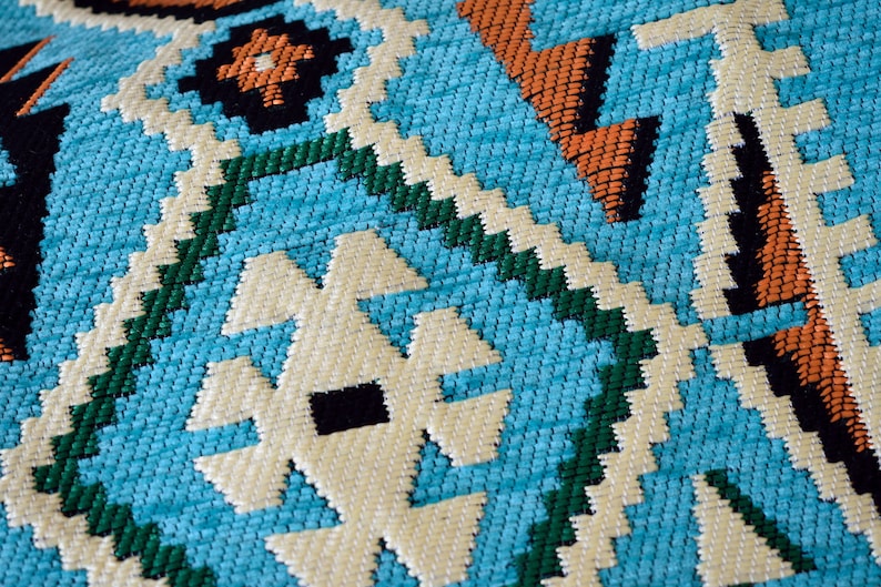 May include: Close-up of a blue, green, white, and orange woven fabric with a geometric pattern.