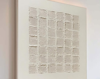 Puede incluir: Gran obra de arte abstracta cuadrada con un patrón texturizado en forma de cuadrícula en tonos beige y crema. La obra está colgada en una pared blanca en un salón moderno, complementada con un sofá y un otomán de tonos neutros.