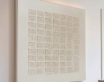 Puede incluir: Una gran obra de arte abstracta texturizada cuadrada de color blanquecino cuelga de una pared blanca. La obra de arte presenta un patrón de rejilla de formas rectangulares en relieve. La habitación incluye un sofá seccional de color claro, una otomana rectangular y un suelo de madera.