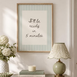 Può includere: Una stampa artistica da parete incorniciata con strisce verticali azzurre e bianche e il testo "I'll be ready in 5 minutes" in un carattere corsivo grigio scuro su sfondo crema, esposta in una cornice di legno chiaro.