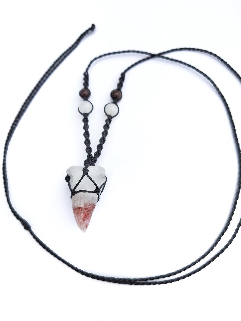Puede incluir: Un collar hecho a mano con un colgante de cristal transparente con tonos rojos y blancos, sujeto en un tejido de macram&eacute; negro. El collar incluye un cord&oacute;n negro y peque&ntilde;as cuentas de madera y blancas. El colgante mide aproximadamente 3,8 cm de largo.