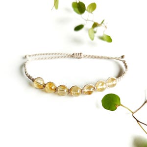 May include: A simple bracelet with a beige cord and a row of golden yellow citrine beads.
