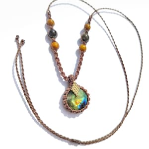 May include: A brown macrame necklace featuring a round, faceted labradorite pendant with a gold-toned textured metal accent. The cord is decorated with alternating round yellow and dark grey beads, secured with a knotted brown string design.