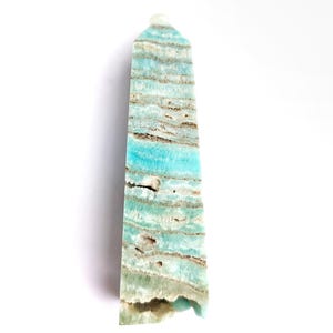 May include: A tall, rectangular gemstone obelisk with a flat top. The stone features bands of turquoise, white, and brown hues. The obelisk is displayed against a white background.