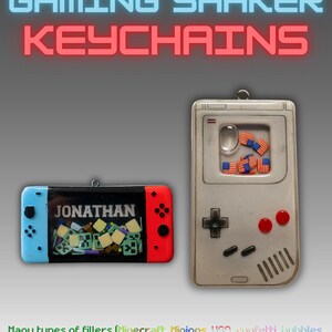 Pode incluir: Dois porta-chaves shaker de jogos. Um é um comando retangular azul e vermelho com o nome JONATHAN e enchimentos quadrados verdes. O outro é uma consola portátil cinzenta com um ecrã contendo pequenos amuletos de bandeiras dos EUA e uma bolha.