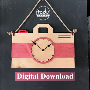 Puede incluir: Una descarga digital de un diseño de reloj con forma de cámara en los formatos DXF, CDR, PDF, SVG, EPS y AI. La esfera del reloj es de color marrón claro con agujas negras y un borde rojo. El cuerpo de la cámara es de color marrón claro con rayas rojas. El diseño está etiquetado como "tozlu desing" y "Descarga digital".
