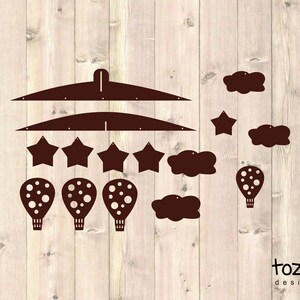 Puede incluir: Un m&oacute;vil de madera marr&oacute;n con un marco colgante, tres globos aerost&aacute;ticos, cinco estrellas y cuatro nubes. El m&oacute;vil est&aacute; dise&ntilde;ado para una guarder&iacute;a o una habitaci&oacute;n infantil.