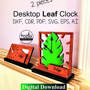 Puede incluir: Dos relojes de mesa de madera con forma de hoja, uno con un diseño de hoja verde y el otro con un diseño rectangular simple. Ambos relojes tienen manecillas negras y un marco negro. Los relojes están sobre una superficie de madera. El texto "2 piezas" está en la parte superior de la imagen. El texto "Desktop Leaf Clock" está debajo del texto "2 piezas". El texto "DXF, CDR, PDF, SVG, EPS, AI" está debajo del texto "Desktop Leaf Clock". El texto "toztu desing" está en un círculo debajo del texto "DXF, CDR, PDF, SVG, EPS, AI". El texto "Rakiye" está en la parte inferior de cada reloj. El texto "Descarga digital" está en la parte inferior de la imagen.
