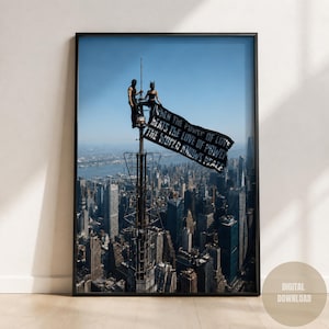 May include: A framed wall art print featuring two figures standing atop a tall antenna spire overlooking a dense city skyline. A black flag waves from the spire with the white text: When the power of love beats the love of power the world knows peace.