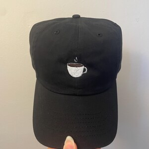 May include: Black baseball cap with a white embroidered coffee cup design.