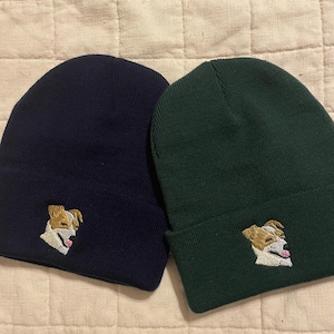 May include: Two knit beanies, one navy blue and one dark green, with an embroidered image of a dog on each.