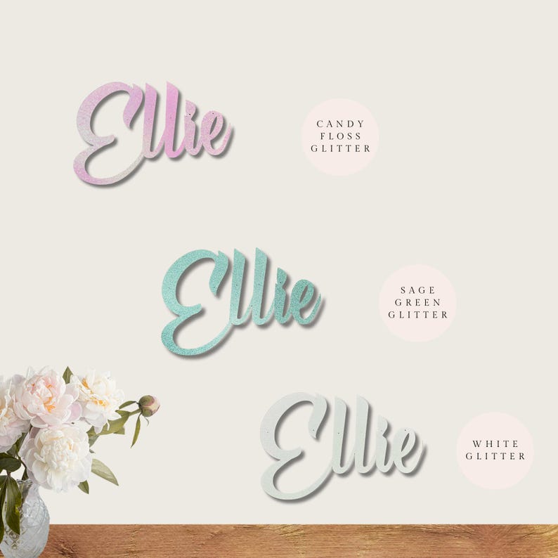 May include: Three versions of the name "Ellie" in cursive script, each with a different glitter finish: candy floss, sage green, and white.