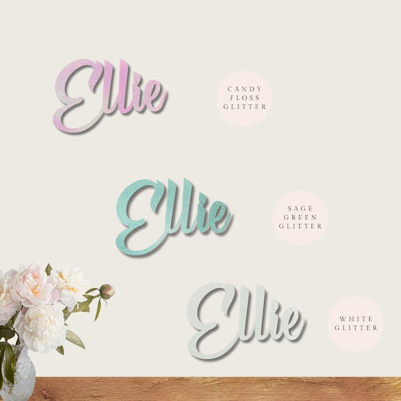 May include: Three versions of the name "Ellie" in cursive script, each with a different glitter finish: candy floss, sage green, and white.