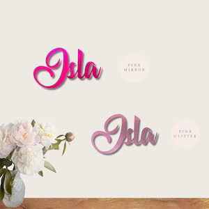 Puede incluir: Dos versiones del nombre "Isla" en rosa. La versi&oacute;n superior es un acabado de espejo rosa. La versi&oacute;n inferior es un acabado de purpurina rosa.
