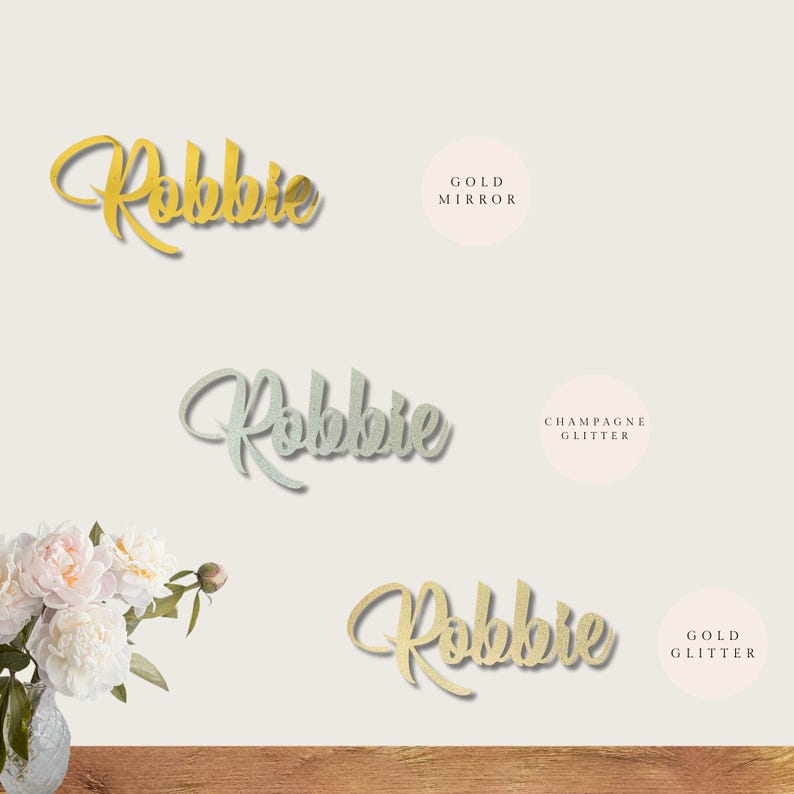 May include: Three versions of the name "Robbie" in different finishes: gold mirror, champagne glitter, and gold glitter. The name is written in a cursive script font.