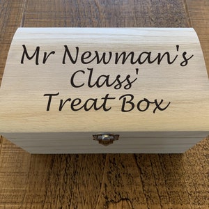 May include: A wooden box with a hinged lid and a metal clasp. The box is engraved with the text "Mr Newman's Class' Treat Box".