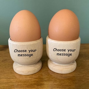 May include: Two wooden egg cups with brown eggs inside. The egg cups have the text "Choose your message" engraved on them.