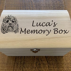 Peut inclure: Une boîte à souvenirs en bois avec un couvercle à charnières et un fermoir en métal. La boîte est gravée du texte "Luca's Memory Box" et d'une image en noir et blanc d'un chien.