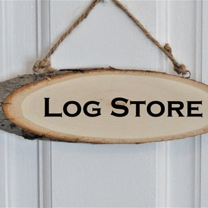 以下が含まれることがあります： 木の看板で、素朴な樹皮の縁取りがあり、黒い文字で「LOG STORE」と書かれています。