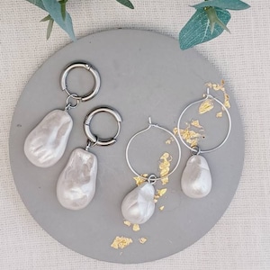 May include: Three pairs of pearl earrings with silver hoops. The earrings are on a grey surface with gold flecks.