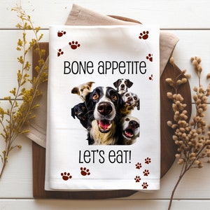 May include: White kitchen towel with a black and white photo of multiple dogs with the text "Bone appetite let's eat!" and brown paw prints.