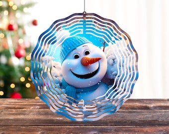 Könnte beinhalten: Ein blauer und weißer Windfänger aus Metall mit einem lächelnden Schneemann-Design. Der Schneemann trägt einen blauen Hut und einen Schal. Der Windfänger hat eine runde Form mit mehreren Metallschichten.