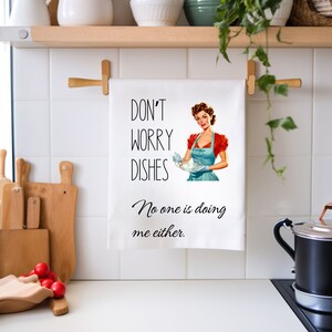 May include: White kitchen towel with a retro illustration of a woman washing dishes. The text reads "Don't worry dishes, No one is doing me either."