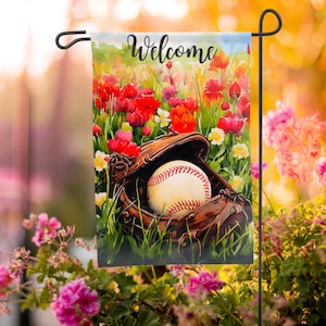 Puede incluir: Una bandera de jardín de bienvenida con una pelota de béisbol y un guante en un campo de flores rojas, amarillas y blancas. El texto "Bienvenido" está impreso en la bandera.