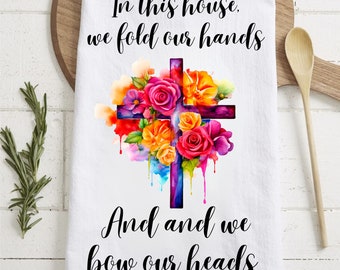 May include: White kitchen towel with a colorful watercolor cross and flowers. The text "In this house, we fold our hands and we bow our heads" is printed on the towel.