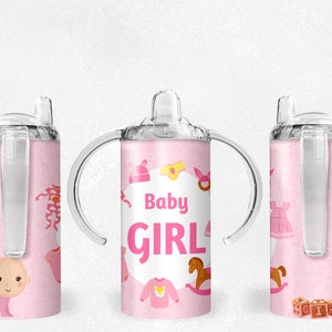May include: Three pink and clear plastic sippy cups with a baby girl theme. The cups have a straw and two handles. The cups are decorated with a pink background and images of baby clothes, a rocking horse, and the words "Baby Girl".