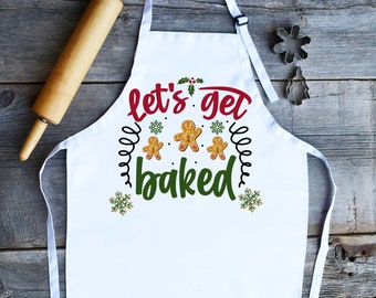 Könnte beinhalten: Weiße Schürze mit dem Text "Let's get baked" in grüner und roter Schrift. Auf der Schürze sind Lebkuchenmänner und Schneeflocken abgebildet.