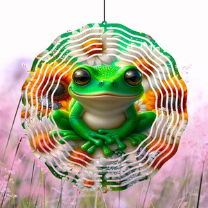 May include: A green frog with a happy expression sits in the center of a metal wind spinner. The spinner is decorated with white daisies and orange sunflowers. The background is a field of pink wildflowers.