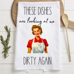 May include: White kitchen towel with a retro illustration of a woman in a red and white apron. The text reads "These dishes are looking at me dirty again."