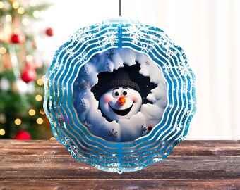 Könnte beinhalten: Ein blauer Windfänger aus Metall mit einem Schneemann-Gesicht in der Mitte. Der Schneemann lächelt und trägt einen schwarzen Hut. Der Windfänger hat ein Schneeflocken-Design.
