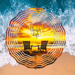 Peut inclure: Un mobile en métal avec un design circulaire représentant une scène de coucher de soleil avec deux chaises sur une plage. Le texte "Beach Life" est écrit en cursive sur le mobile.
