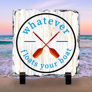May include: A white wooden sign with a black circle and the text "whatever floats your boat" in blue. Two crossed orange paddles are inside the circle.