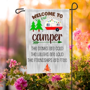 Puede incluir: Un letrero de madera blanco con el texto "WELCOME TO our camper THE DRINKS are COLD THE LAUGHS are LOUD THE FRIENDSHIPS are Free" y una imagen de dibujos animados de una autocaravana roja con árboles verdes y una fogata.