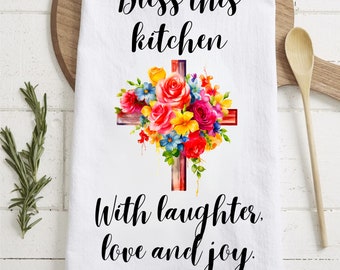 May include: White kitchen towel with a floral cross design and the text "Bless this kitchen with laughter, love and joy."