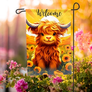 Könnte beinhalten: Eine Willkommens-Gartenflagge mit einer niedlichen Cartoon-Highland-Kuh mit einem flauschigen orangefarbenen Fell, die auf einem Sonnenblumenfeld steht. Die Flagge hat einen gelben Hintergrund mit einer Sonne und dem Wort "Willkommen" in schwarzer Schrift.