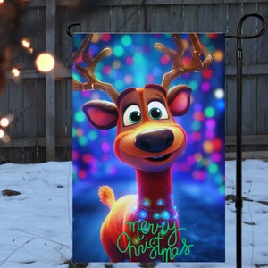 Puede incluir: Una bandera de jardín navideña con un reno de dibujos animados con la nariz roja y cuernos. El reno está rodeado de luces de colores y el texto "merry christmas" está escrito en verde.