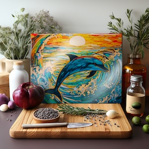 May include: A colorful glass cutting board with a stained glass style image of a dolphin jumping out of the water. The dolphin is blue, the water is blue and green, and the sky is orange and yellow. The cutting board is on a wooden surface with a sprig of rosemary and some black peppercorns.