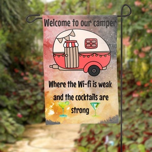 May include: A colorful garden flag with a cartoon camper van and the text "Welcome to our camper Where the Wi-fi is weak and the cocktails are strong".