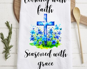 May include: White kitchen towel with a blue cross surrounded by blue flowers and the text "Cooking with faith, Seasoned with grace".