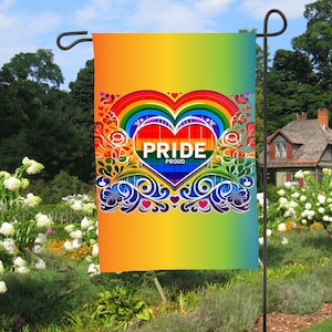 Puede incluir: Una bandera de jardín con un diseño de corazón arcoíris. El corazón tiene las palabras "Pride Proud" en su interior. La bandera es amarilla y verde con un arcoíris sobre el corazón.