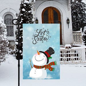 Puede incluir: Una bandera de jardín azul y blanca con un muñeco de nieve y el texto "Let it Snow". El muñeco de nieve lleva un sombrero de copa negro, una bufanda roja y verde y tiene una nariz de zanahoria.