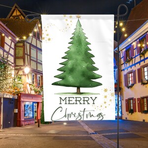 May include: A white Christmas-themed garden flag with a green watercolor illustration of a Christmas tree and the text "Merry Christmas".