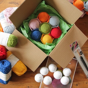 May include: A cardboard box filled with colorful yarn balls and crocheted balls. The box also contains a crochet hook and a small bag of white balls. The yarn balls are in shades of red, orange, yellow, green, blue, and pink.