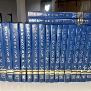 Może przedstawiać: Kolekcja niebieskich książek w twardej oprawie zatytułowanych "The New Book of Knowledge". Grzbiety są niebieskie ze złotymi literami i numeracją. Książki ułożone są w rzędzie, z kilkoma dodatkowymi tomami ułożonymi na wierzchu.